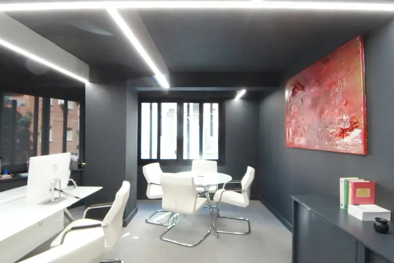 Despacho con mesa de trabajo, mesa redonda y un cuadro rojo en la pared