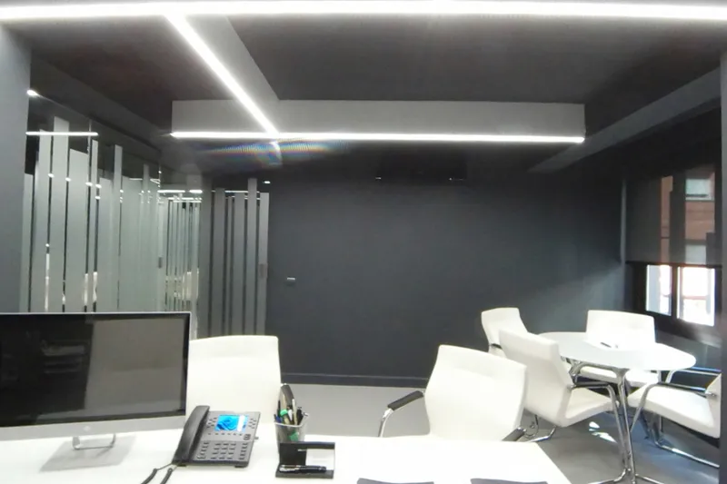 Despacho con pantallas en la mesa de trabajo y mesa redonda con sillas blancas