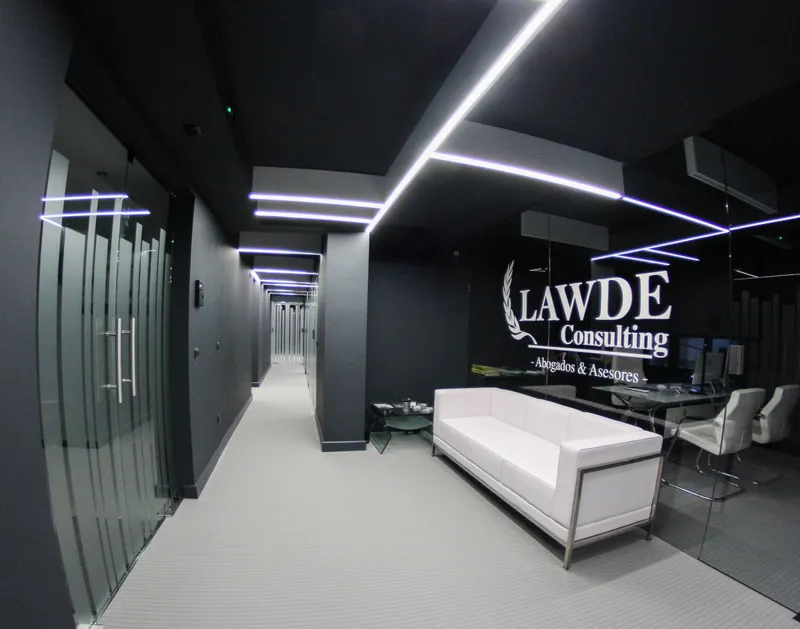 La recepción de LAWDE: el logotipo en la mampara de cristal, el sofá blanco y, al fondo, el pasillo con líneas de luz en el techo