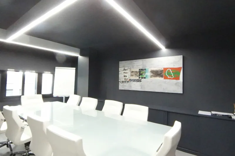 La sala de juntas: mesa blanca alargada con sillas blancas, un cuadro y el rotafolio