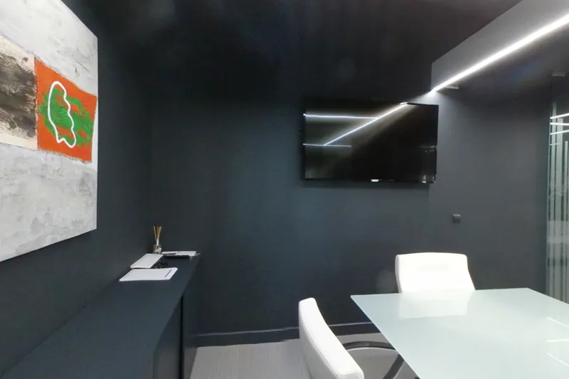La sala de juntas, con la pantalla en la pared y la mesa blanca de reuniones